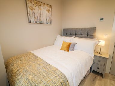 A bedroom with a bed a gray headboard a bedside table with a lamp and a painting on the wall at The Beachhouse in Meenlaragh near Gortahork County Donegal