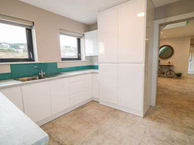 A kitchen with white cabinets a sink and two windows showing a view outside at The Beachhouse Meenlaragh near Gortahork County Donegal