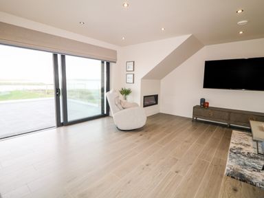 A living room with sliding glass doors and a reclining chair facing a wall mounted TV at The Beachhouse in Meenlaragh near Gortahork County Donegal