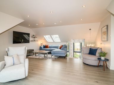 A living room with a wall-mounted TV a blue sectional sofa a round armchair wooden floor and skylight windows at The Beachhouse in Meenlaragh near Gortahork County Donegal