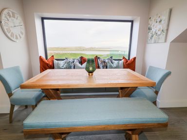 A dining area with a wooden table surrounded by blue chairs and bench and a large window showing a landscape at The Beachhouse in Meenlaragh near Gortahork County Donegal