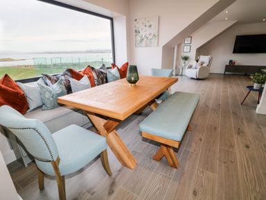 A dining area with a wooden table blue chairs and bench by a large window with cushions at The Beachhouse in Meenlaragh near Gortahork County Donegal