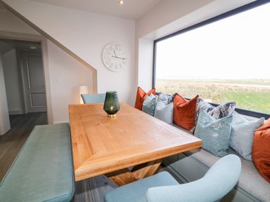A dining area with a wooden table, blue chairs, a bench with cushions, and a large window at The Beachhouse in Meenlaragh near Gortahork County Donegal