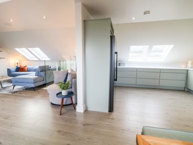 A modern open space with a blue sectional sofa and grey armchair next to a kitchen with light-colored cabinets and wooden flooring at The Beachhouse in Meenlaragh near Gortahork County Donegal