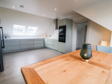 A kitchen with gray cabinets, two skylight windows, an oven, and a wooden dining table with a green textured lamp at The Beachhouse in Meenlaragh near Gortahork County Donegal
