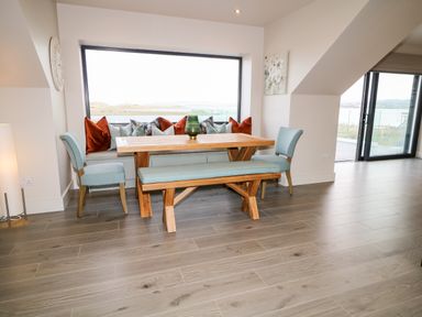 A dining area with a wooden table bench and chairs by a large window at The Beachhouse in Meenlaragh near Gortahork County Donegal