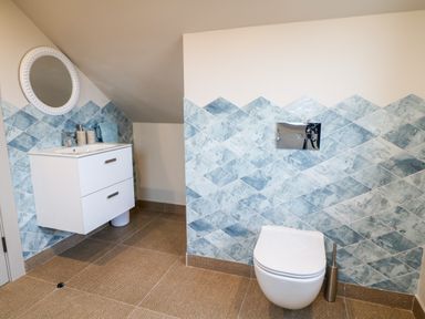 A bathroom with a wall-mounted toilet and a sink with a round mirror at The Beachhouse in Meenlaragh near Gortahork County Donegal
