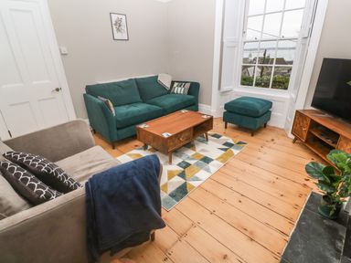 A living room with green and grey sofas a wooden coffee table a patterned rug and a television on a wooden stand at Belmont in Newlyn
