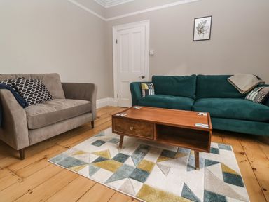A living room with a green sofa a beige armchair a wooden coffee table and a geometric patterned rug at Belmont in Newlyn