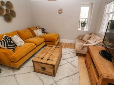 A living room with a mustard yellow sofa and beige armchair and wooden coffee table at Belmont in Newlyn