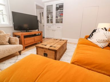 A living room with an orange sofa a wooden coffee table a TV on a wooden stand and a beige armchair at Belmont in Newlyn