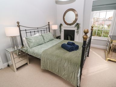 A bedroom with a metal bed frame and green bedding with two lamps on mirrored nightstands at Belmont in Newlyn