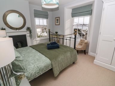 A bedroom with a bed a round mirror on the wall and two windows at Belmont in Newlyn