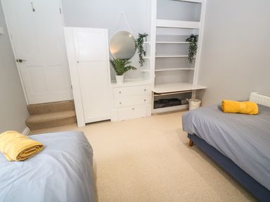 A bedroom with two single beds with gray bedding and yellow towels on top a white dresser with round mirror and plants built in shelves and carpeted floor at Belmont in Newlyn