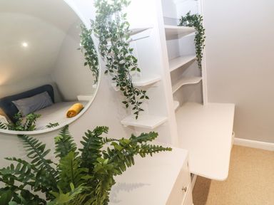 A white desk with shelves and green plants next to a round mirror reflecting a bed with a yellow towel at Belmont in Newlyn