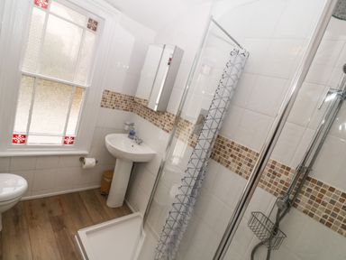 A bathroom with a corner shower enclosure a pedestal sink a toilet and a frosted window with stained glass accents at Belmont in Newlyn