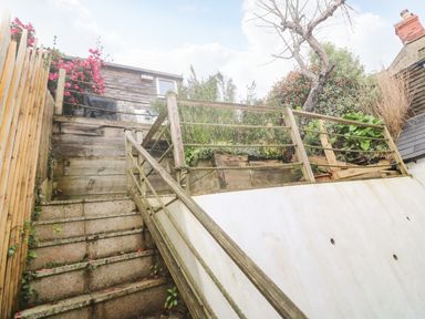 An outdoor staircase with wooden railing leading to a raised garden area with plants and a tree at Belmont in Newlyn