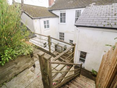 An outdoor staircase with wooden railing leading down to a paved area beside white buildings with windows at Belmont Newlyn