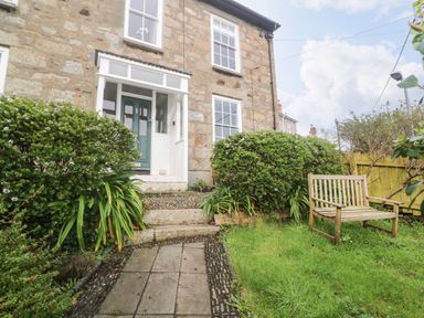 A stone house entrance with green plants and a wooden bench in the garden at Belmont in Newlyn