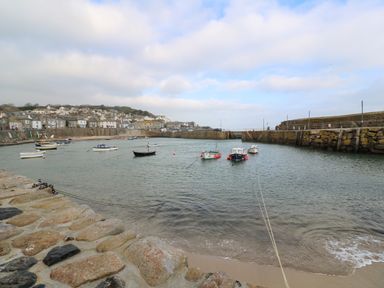 A small harbor with boats moored in the water and stone walls surrounding it with houses in the background at Belmont in Newlyn