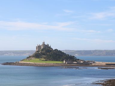 An island with a castle and trees surrounded by water and hills in the background at Belmont in Newlyn