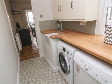 A narrow utility room with patterned floor tiles washing machine dishwasher and wooden countertop at Belmont in Newlyn