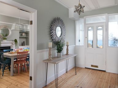 An entryway with a wooden console table holding two candles and a plant and a round decorative mirror on the wall at Belmont in Newlyn