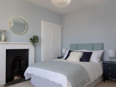 A bedroom with a bed pillows and two nightstands next to a fireplace and closet at Belmont in Newlyn