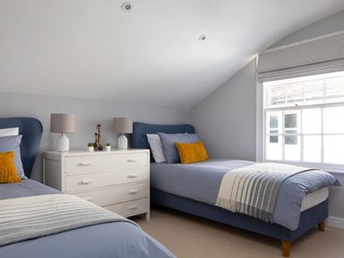 A bedroom with two single beds side by side with a white chest of drawers and window at Belmont in Newlyn