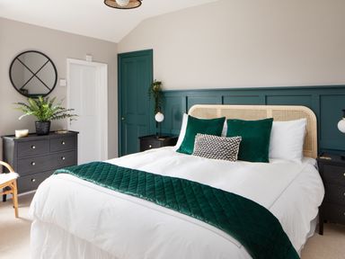 A bedroom with a bed featuring white bedding and green pillows beside black dressers and a round wall mirror at Belmont in Newlyn