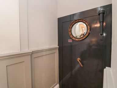 A close up of a black metal vault door with a round window and handle in a hallway at The Vault House in Bellingham