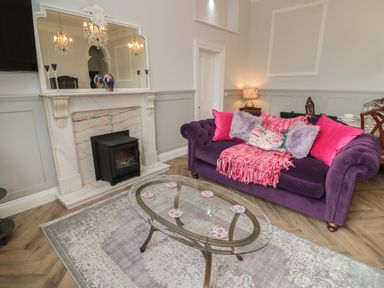A living room with a purple sofa pink cushions a glass coffee table and a fireplace at The Vault House in Bellingham
