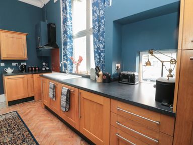 A kitchen with wooden cabinets a black countertop a sink a window with blue floral curtains and various kitchen appliances at The Vault House in Bellingham