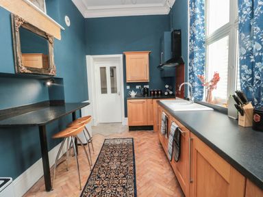 A kitchen with wooden cabinets a black countertop two stools and blue floral curtains at The Vault House in Bellingham