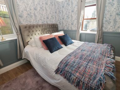 A bedroom with a bed covered in pillows and a blanket near two windows with curtains at The Vault House in Bellingham