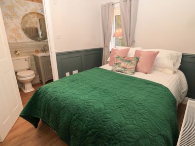 A bedroom with a green quilted bedspread and a bathroom with floral wallpaper at The Vault House in Bellingham