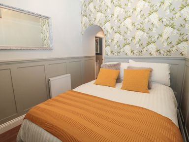 A bedroom with a bed featuring yellow pillows and a blanket floral wallpaper and a mirror at The Vault House in Bellingham