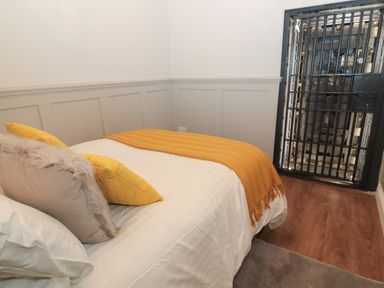 A bedroom with a bed and yellow pillows next to a black metal barred door at The Vault House in Bellingham