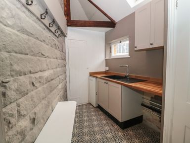 A utility room with a wooden countertop sink white cabinets a stone wall with hooks and patterned floor tiles at The Vault House in Bellingham