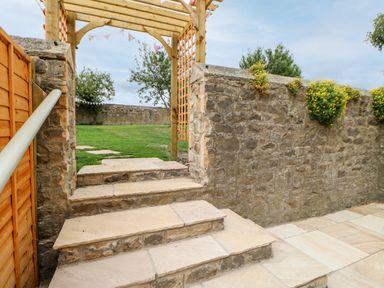Stone steps leading to a wooden pergola and green lawn with trees and stone walls at The Vault House in Bellingham