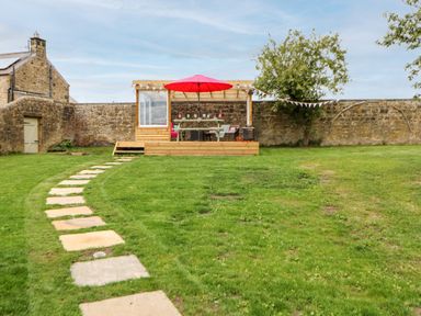 A garden with a stone pathway leading to a wooden patio with a table and red umbrella at The Vault House in Bellingham