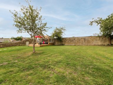 A garden with a tree a wooden deck with picnic table and umbrella and stone walls at The Vault House in Bellingham