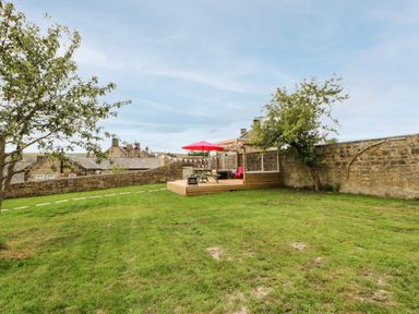 A backyard with green grass a wooden deck with a picnic table and red umbrella surrounded by stone walls at The Vault House in Bellingham