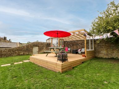 An outdoor wooden deck with a picnic table and red umbrella next to stone walls in a garden at The Vault House in Bellingham