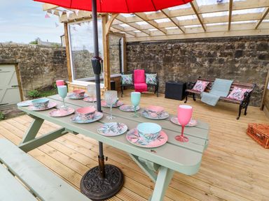 An outdoor covered patio with a picnic table set with plates bowls and glasses next to benches with cushions and throws at The Vault House in Bellingham