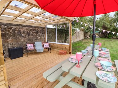 An outdoor covered wooden deck with a bench and a table set with colorful dishes and glasses under a red umbrella at The Vault House in Bellingham
