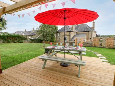 An outdoor wooden deck with a picnic table set with plates and glasses under a red umbrella in a backyard at The Vault House in Bellingham