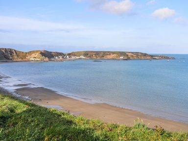 A coastal bay with a sandy beach grass in the foreground and hills with buildings in the background at Min Y Mor - Morfa Nefyn in Morfa Nefyn