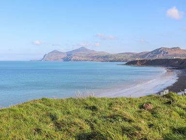 A coastline with a grassy foreground a sandy beach and hills in the distance at Min Y Mor - Morfa Nefyn