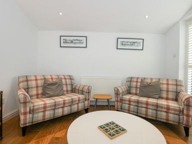 A small living room with two plaid sofas and a round white table with a tic tac toe game at Min Y Mor - Morfa Nefyn